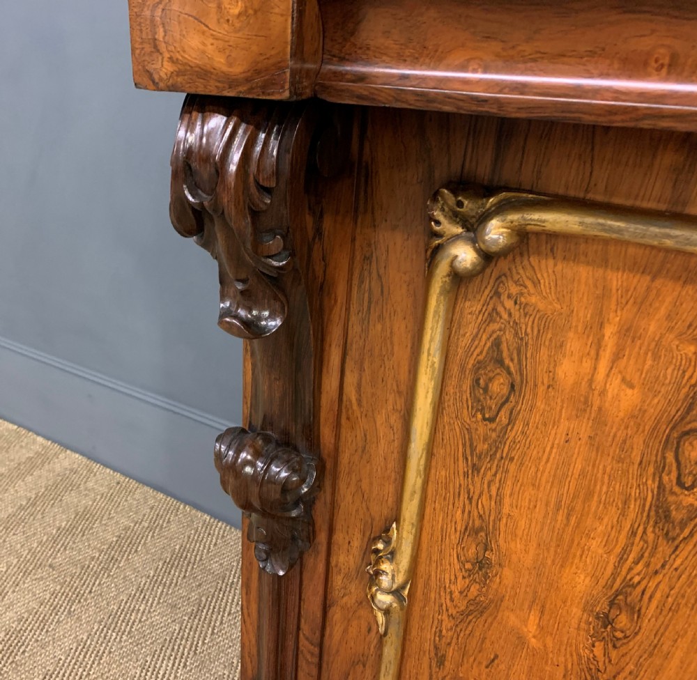 A dark Regency period rosewood side cabinet featuring two cupboard doors with gilded bronze trim and carved scroll supports on a plinth base. View XII