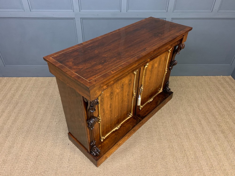 A dark Regency period rosewood side cabinet featuring two cupboard doors with gilded bronze trim and carved scroll supports on a plinth base. View XV