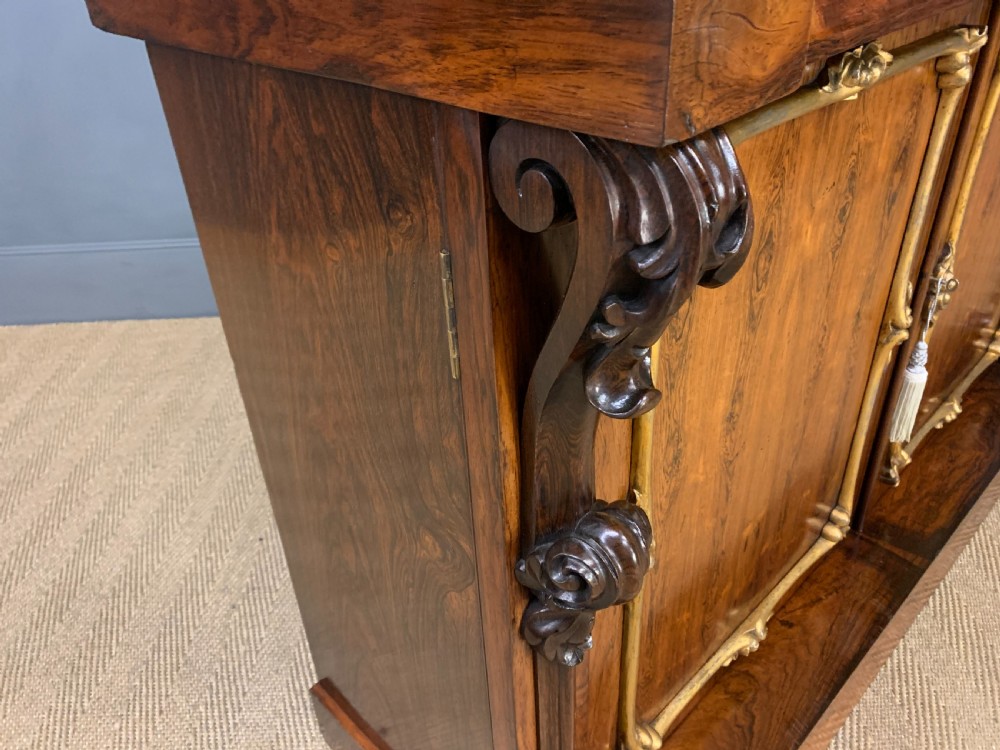 A dark Regency period rosewood side cabinet featuring two cupboard doors with gilded bronze trim and carved scroll supports on a plinth base. View XVII