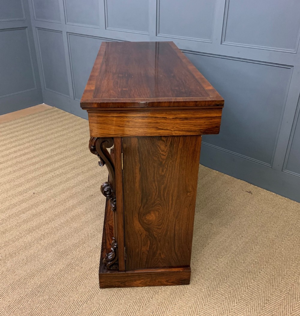 A dark Regency period rosewood side cabinet featuring two cupboard doors with gilded bronze trim and carved scroll supports on a plinth base. View XXII