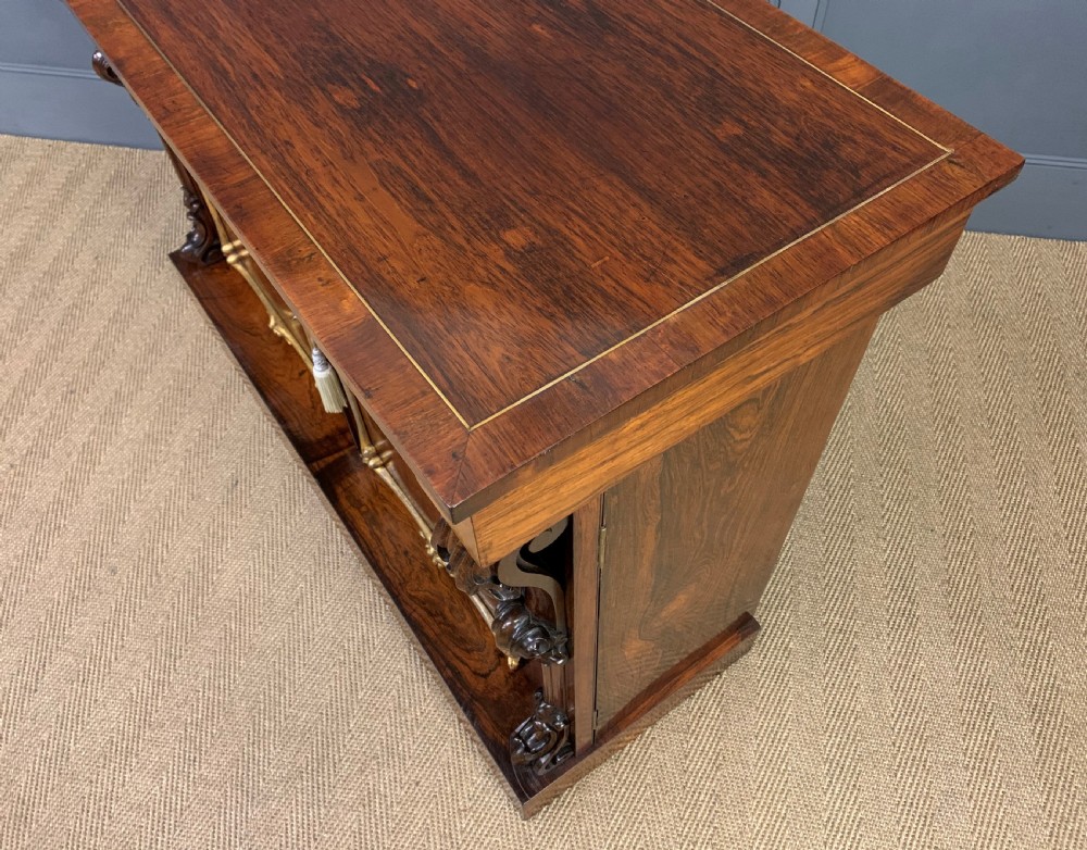 A dark Regency period rosewood side cabinet featuring two cupboard doors with gilded bronze trim and carved scroll supports on a plinth base. View XXIII