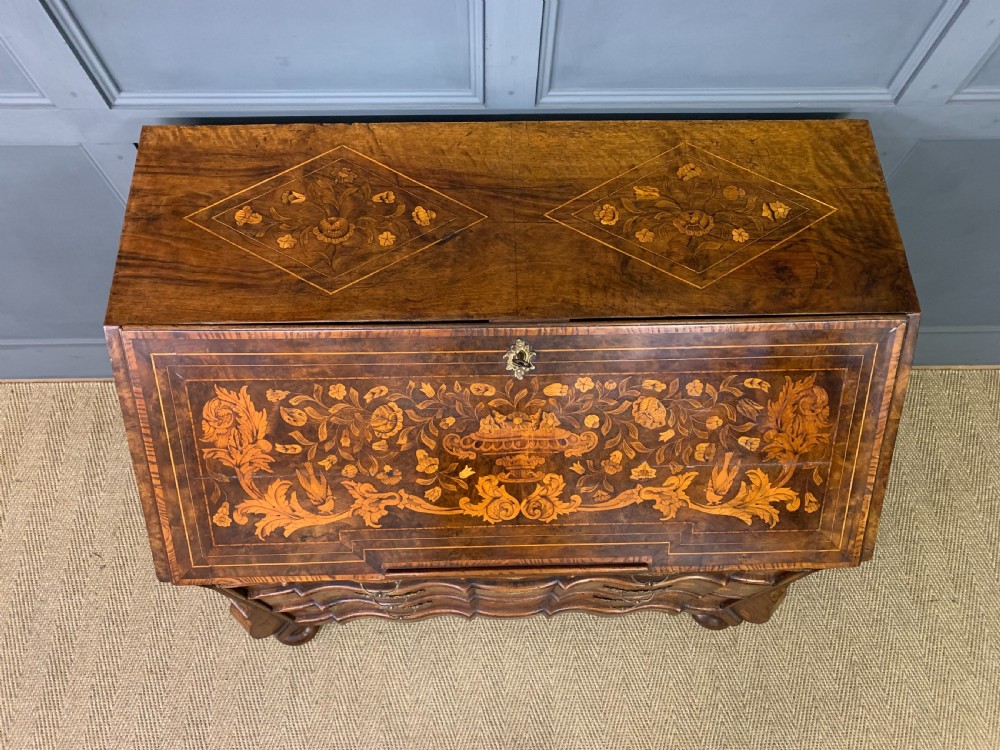 An 18th-century Dutch walnut bureau featuring detailed floral marquetry inlay across the slant-front lid and drawer fronts, accented with brass handles. View IV