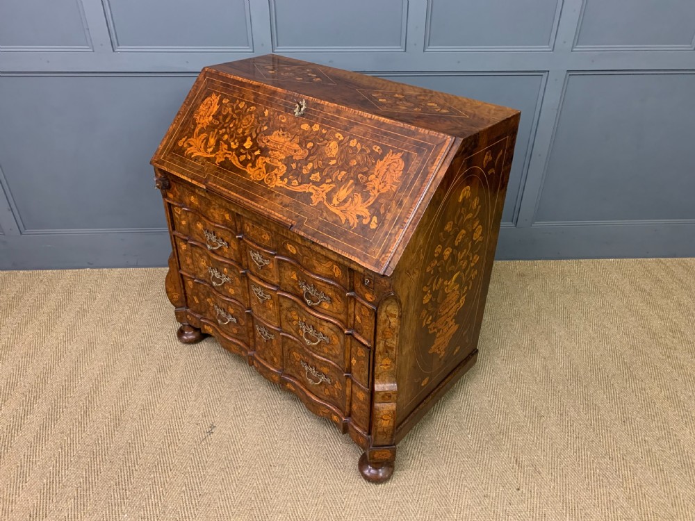 An 18th-century Dutch walnut bureau featuring detailed floral marquetry inlay across the slant-front lid and drawer fronts, accented with brass handles. View XVIII