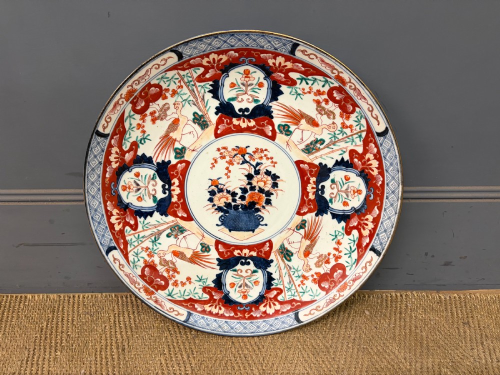 A circular 19th-century Japanese Imari porcelain charger decorated in cobalt blue, iron red, and gilt with paneled bird and floral motifs around a central vase design.