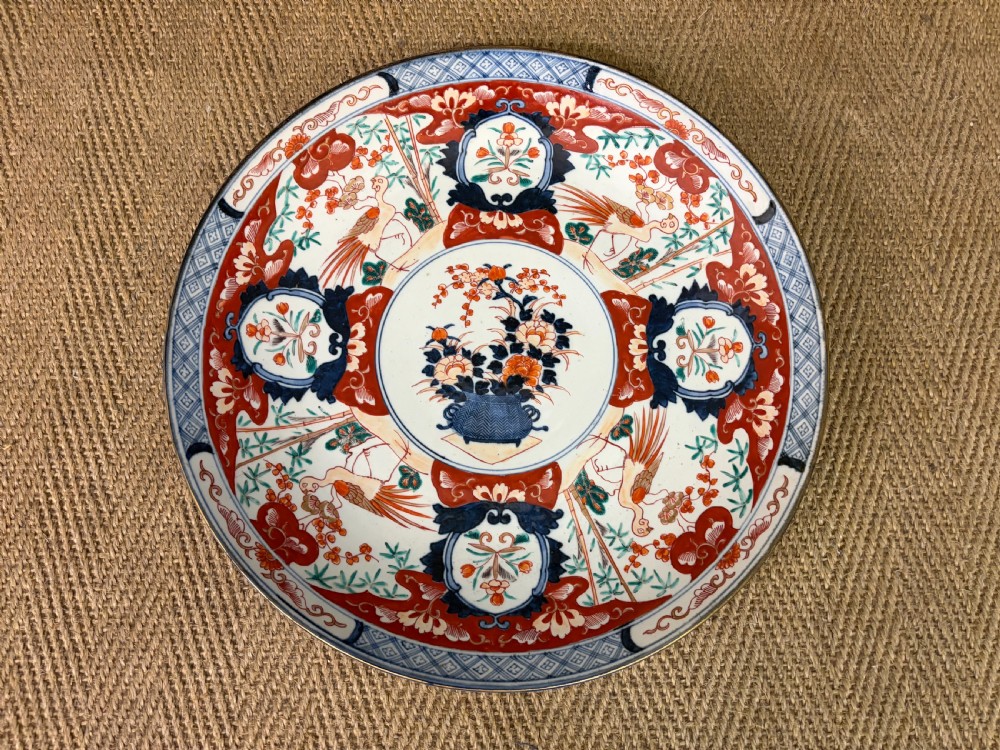 A circular 19th-century Japanese Imari porcelain charger decorated in cobalt blue, iron red, and gilt with paneled bird and floral motifs around a central vase design. View II