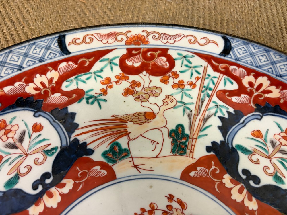 A circular 19th-century Japanese Imari porcelain charger decorated in cobalt blue, iron red, and gilt with paneled bird and floral motifs around a central vase design. View V
