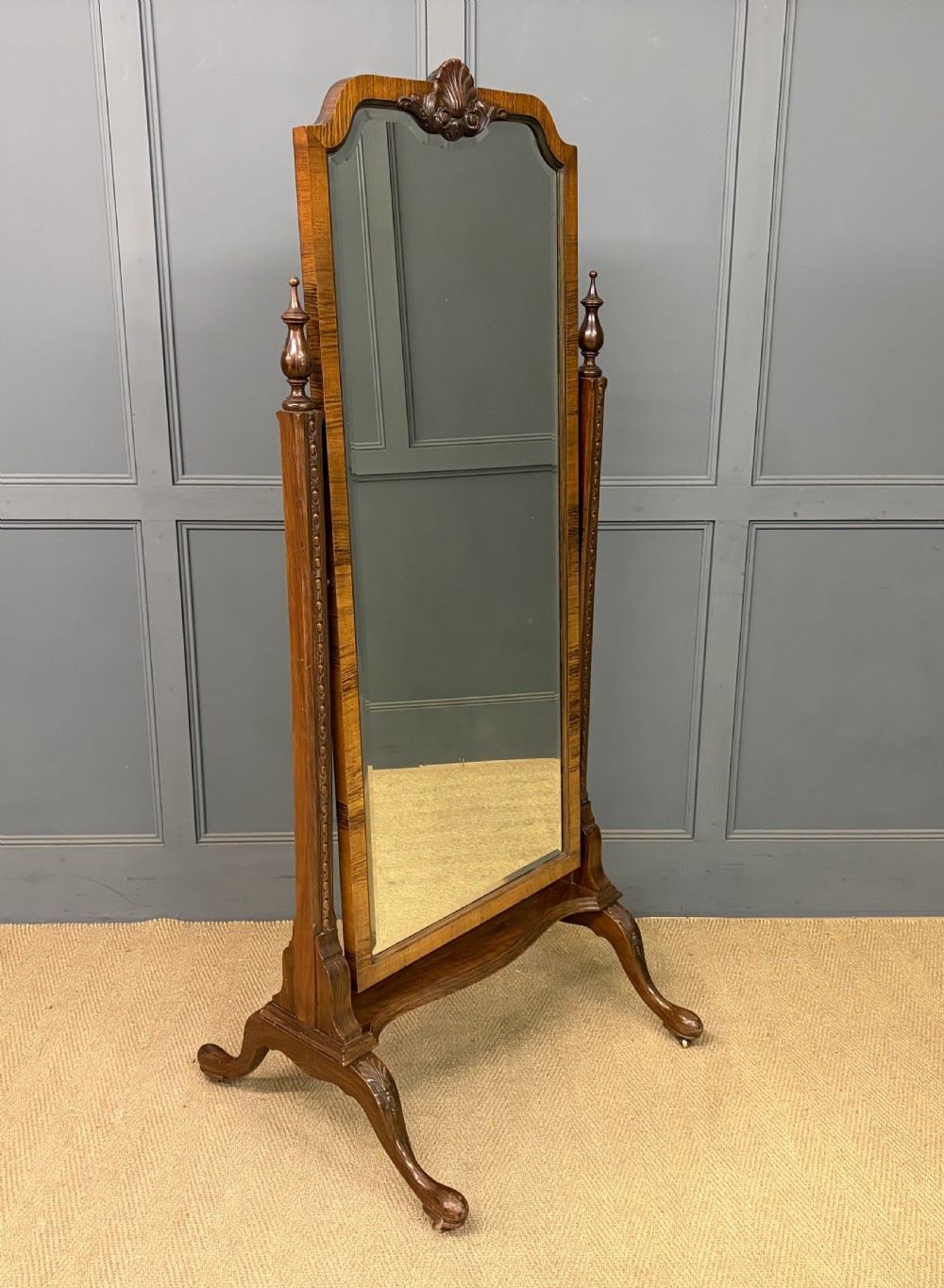 A Queen Anne style walnut cheval mirror with an arched frame, carved shell motif, finial posts, and cabriole legs.