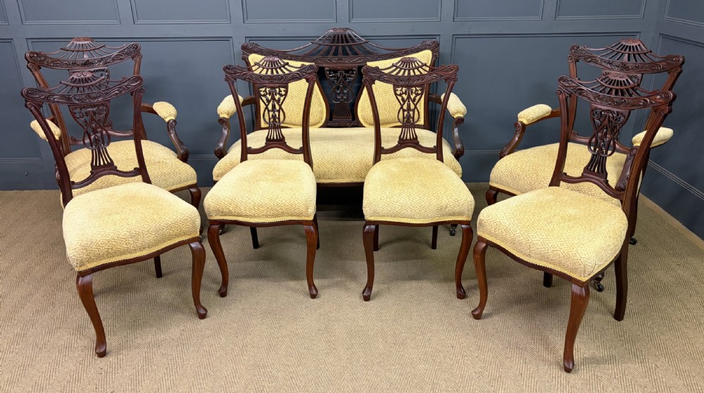A seven-piece Victorian mahogany salon suite comprising a carved settee, two armchairs, and four side chairs, all upholstered in yellow patterned fabric.