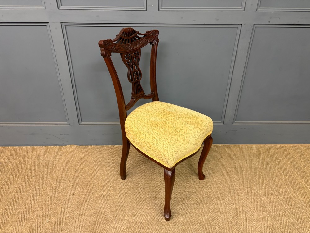 A seven-piece Victorian mahogany salon suite comprising a carved settee, two armchairs, and four side chairs, all upholstered in yellow patterned fabric. View X