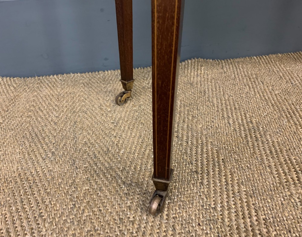 An Edwardian oval mahogany writing table featuring a green leather inset top, single frieze drawer with brass bail handles, and square tapered legs with castors. View VI