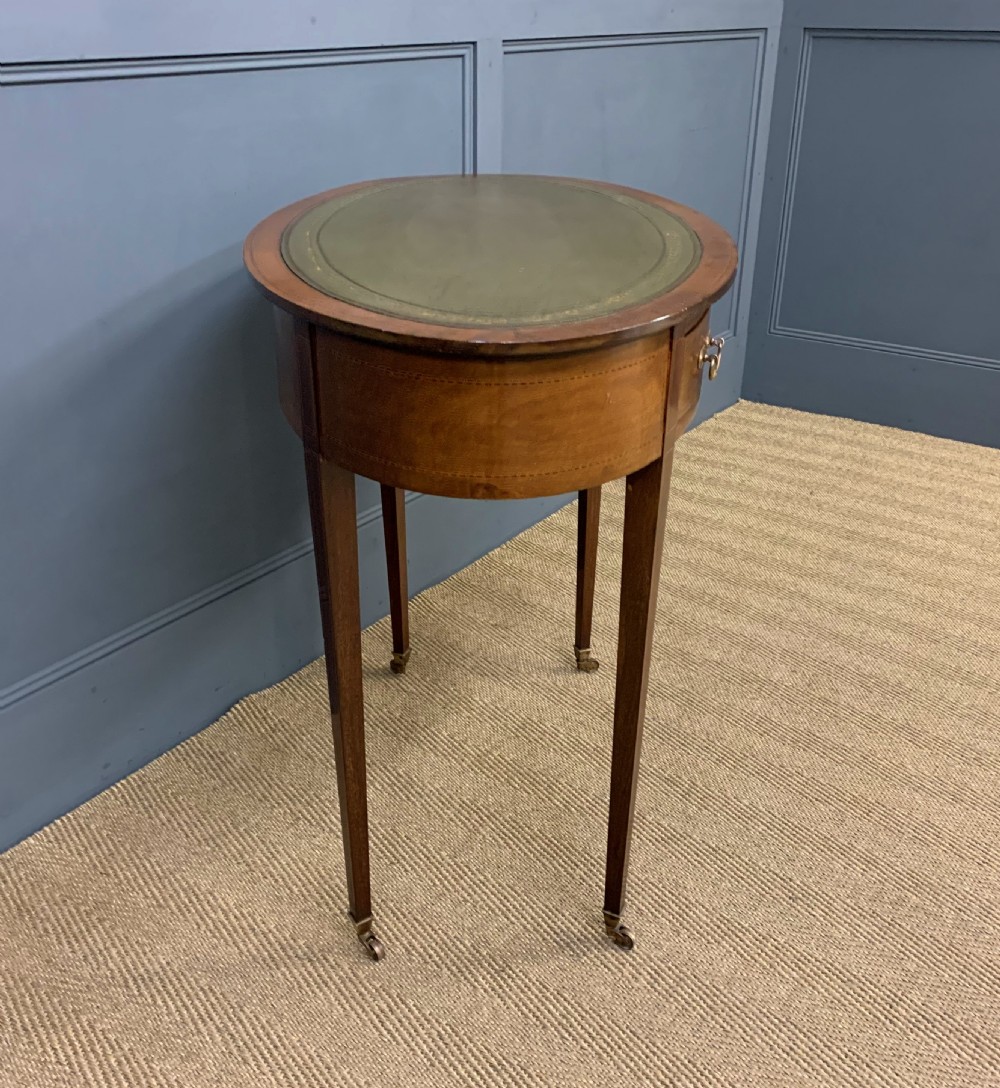 An Edwardian oval mahogany writing table featuring a green leather inset top, single frieze drawer with brass bail handles, and square tapered legs with castors. View X
