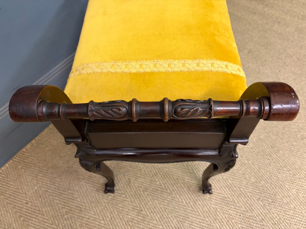 An antique dark mahogany piano stool featuring carved cabriole legs, scroll side handles, a carved shell apron motif, and a padded yellow velvet seat. View VII