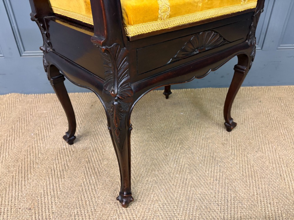 An antique dark mahogany piano stool featuring carved cabriole legs, scroll side handles, a carved shell apron motif, and a padded yellow velvet seat. View VIII