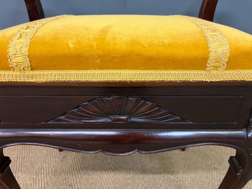 An antique dark mahogany piano stool featuring carved cabriole legs, scroll side handles, a carved shell apron motif, and a padded yellow velvet seat. View XIII