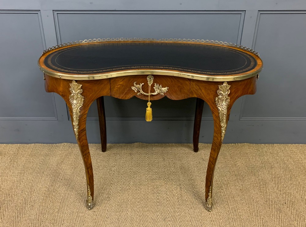 A Victorian kidney-shaped rosewood writing table featuring a dark leather top with gilt tooling, a pierced brass gallery, and cabriole legs with decorative ormolu mounts.