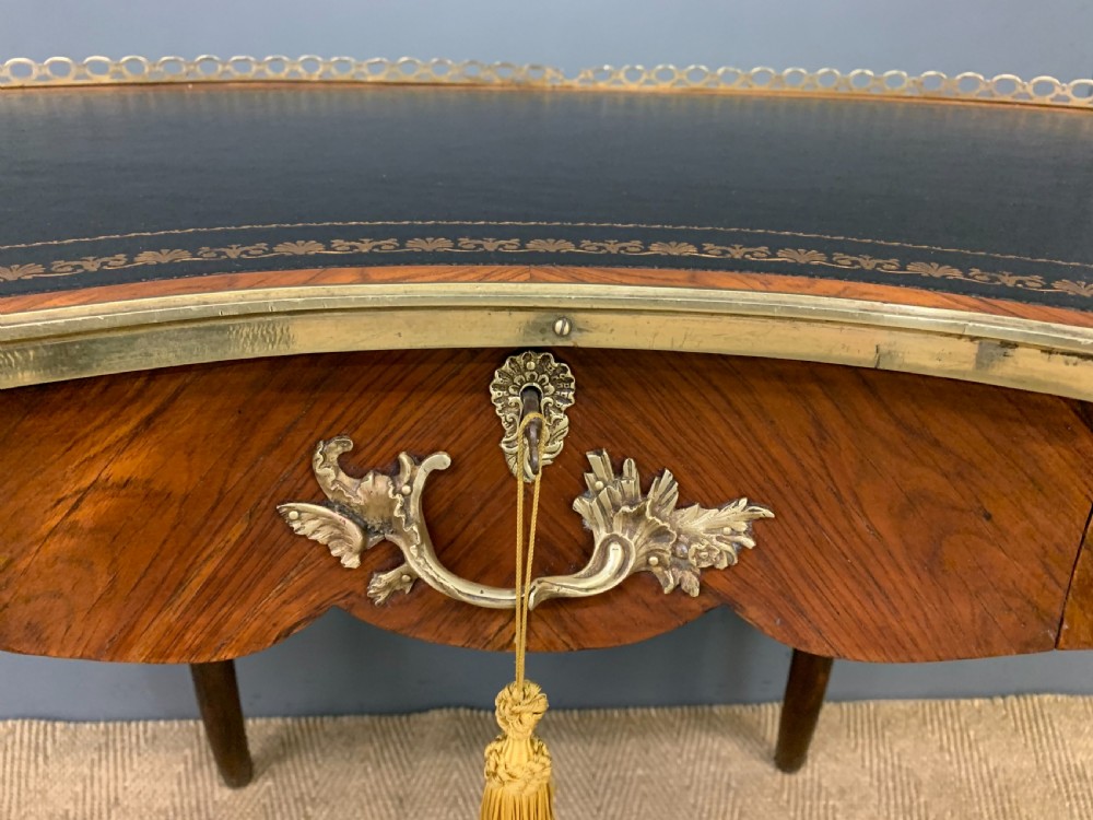 A Victorian kidney-shaped rosewood writing table featuring a dark leather top with gilt tooling, a pierced brass gallery, and cabriole legs with decorative ormolu mounts. View V