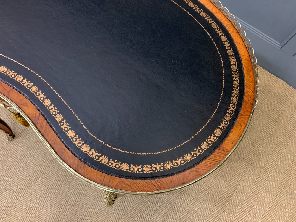 A Victorian kidney-shaped rosewood writing table featuring a dark leather top with gilt tooling, a pierced brass gallery, and cabriole legs with decorative ormolu mounts. View VI