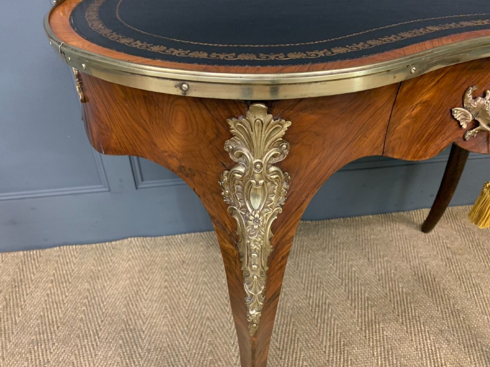 A Victorian kidney-shaped rosewood writing table featuring a dark leather top with gilt tooling, a pierced brass gallery, and cabriole legs with decorative ormolu mounts. View VII