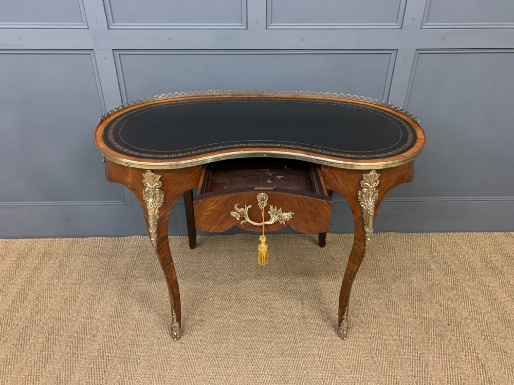 A Victorian kidney-shaped rosewood writing table featuring a dark leather top with gilt tooling, a pierced brass gallery, and cabriole legs with decorative ormolu mounts. View VIII