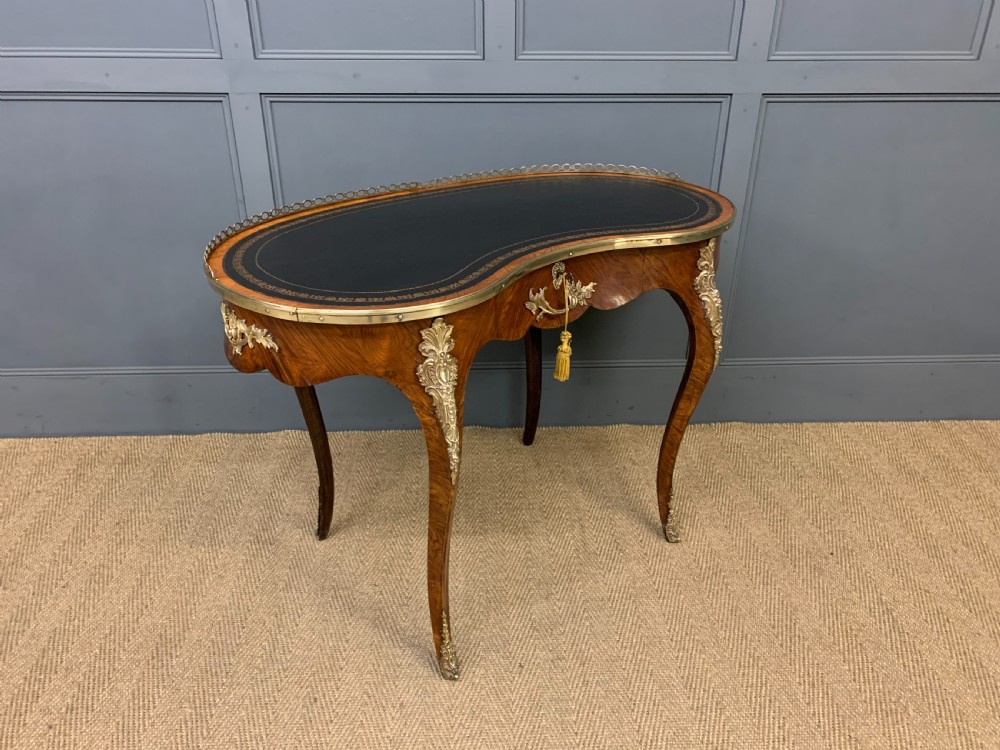 A Victorian kidney-shaped rosewood writing table featuring a dark leather top with gilt tooling, a pierced brass gallery, and cabriole legs with decorative ormolu mounts. View IX