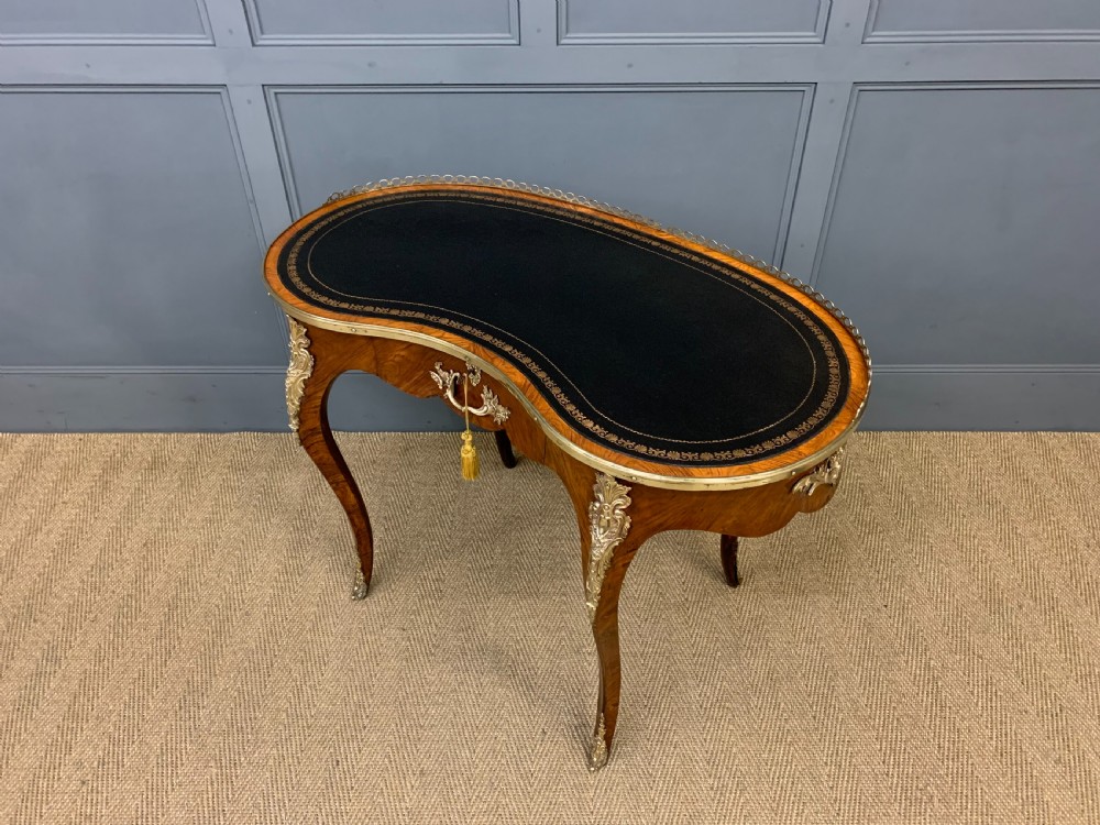 A Victorian kidney-shaped rosewood writing table featuring a dark leather top with gilt tooling, a pierced brass gallery, and cabriole legs with decorative ormolu mounts. View XIV