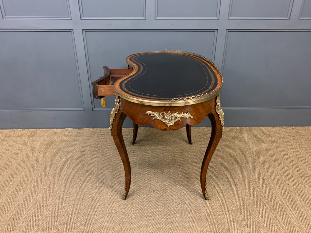 A Victorian kidney-shaped rosewood writing table featuring a dark leather top with gilt tooling, a pierced brass gallery, and cabriole legs with decorative ormolu mounts. View XV