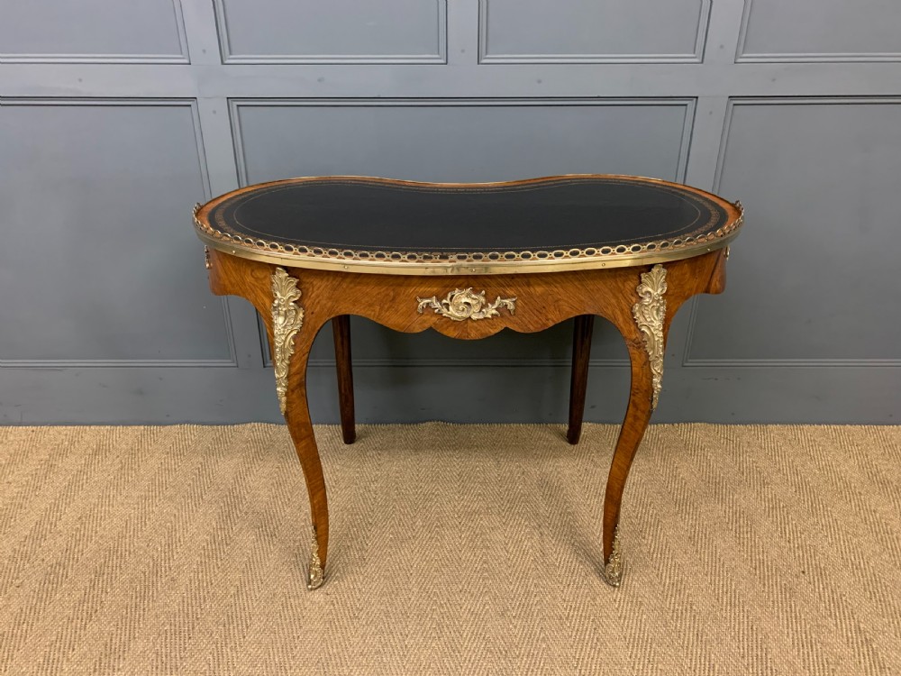 A Victorian kidney-shaped rosewood writing table featuring a dark leather top with gilt tooling, a pierced brass gallery, and cabriole legs with decorative ormolu mounts. View XVI
