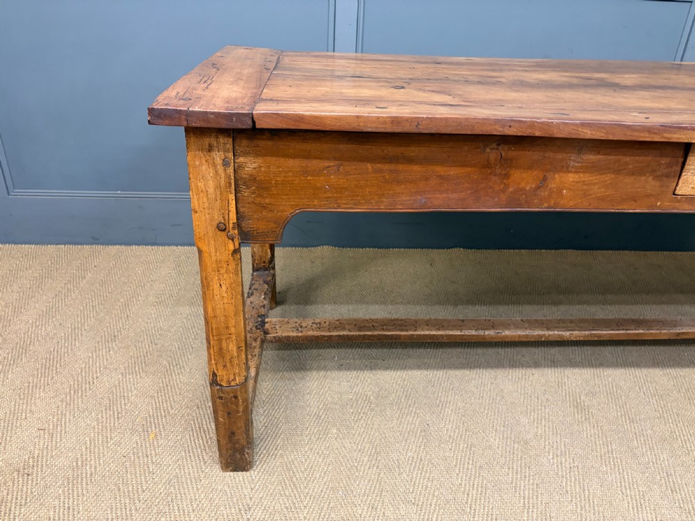 An early 19th-century fruitwood refectory table with a plank top, single side drawer, and stretcher base. View X