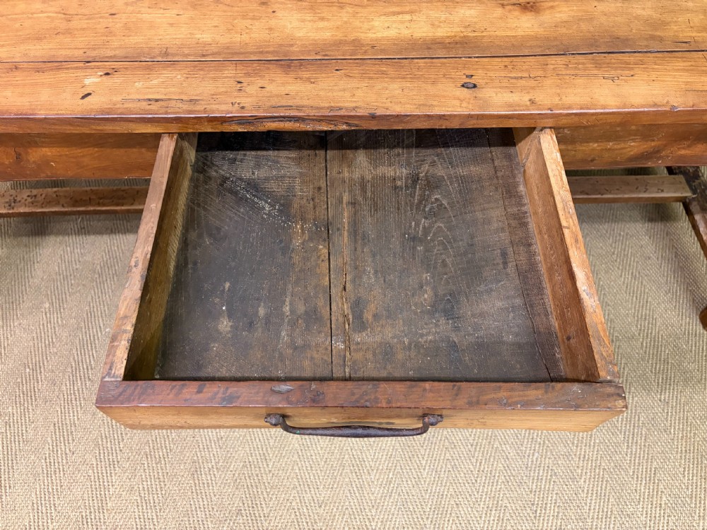 An early 19th-century fruitwood refectory table with a plank top, single side drawer, and stretcher base. View XIII