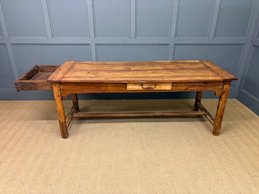 An early 19th-century fruitwood refectory table with a plank top, single side drawer, and stretcher base. View XIV