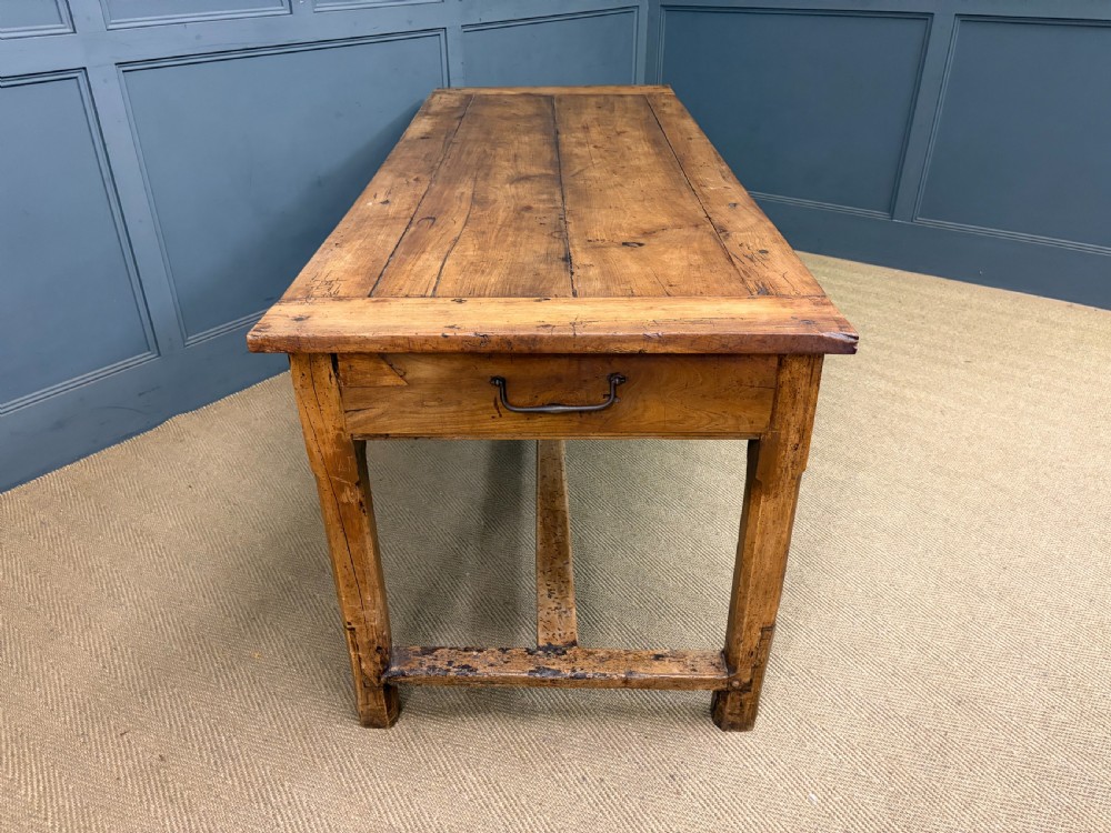 An early 19th-century fruitwood refectory table with a plank top, single side drawer, and stretcher base. View XVI
