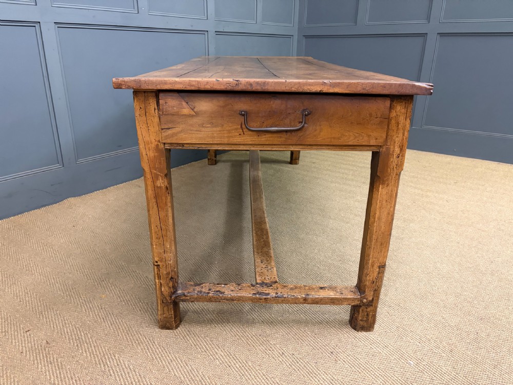 An early 19th-century fruitwood refectory table with a plank top, single side drawer, and stretcher base. View XVII