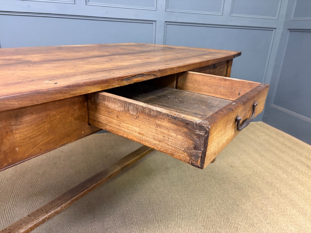 An early 19th-century fruitwood refectory table with a plank top, single side drawer, and stretcher base. View XXII
