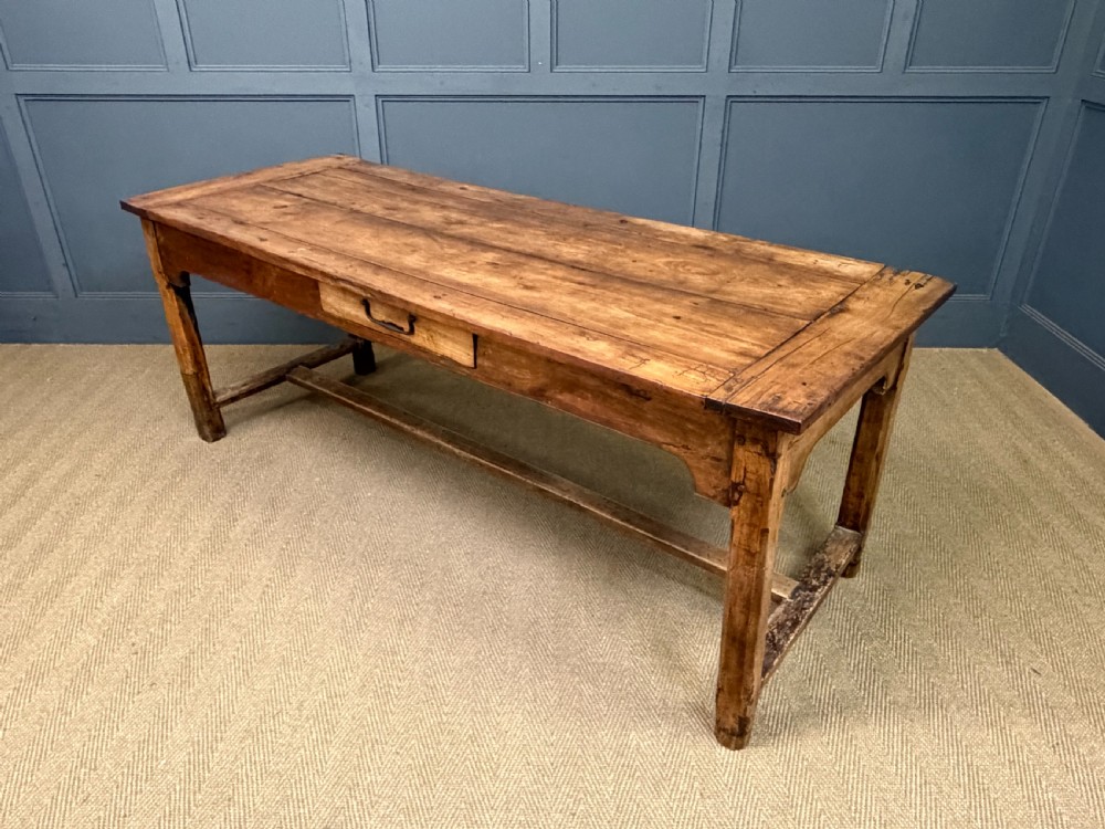 An early 19th-century fruitwood refectory table with a plank top, single side drawer, and stretcher base. View XXIII