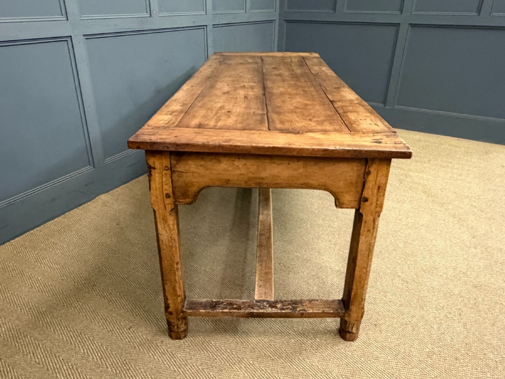 An early 19th-century fruitwood refectory table with a plank top, single side drawer, and stretcher base. View XXVI