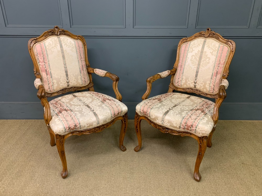 A pair of French carved walnut armchairs featuring cabriole legs and pink and cream patterned fabric upholstery.