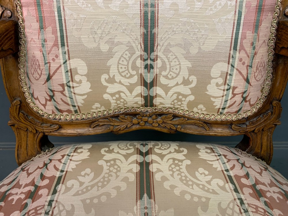 A pair of French carved walnut armchairs featuring cabriole legs and pink and cream patterned fabric upholstery. View X