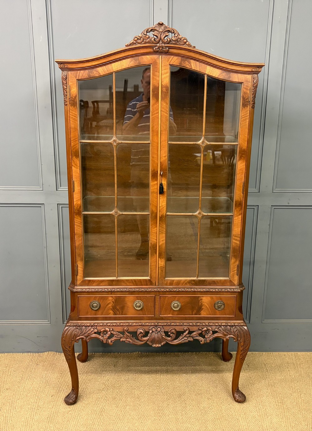 An antique Queen Anne style glazed display cabinet in warm brown wood featuring arched doors with glass panes, drawers with brass handles, and carved cabriole legs. View III