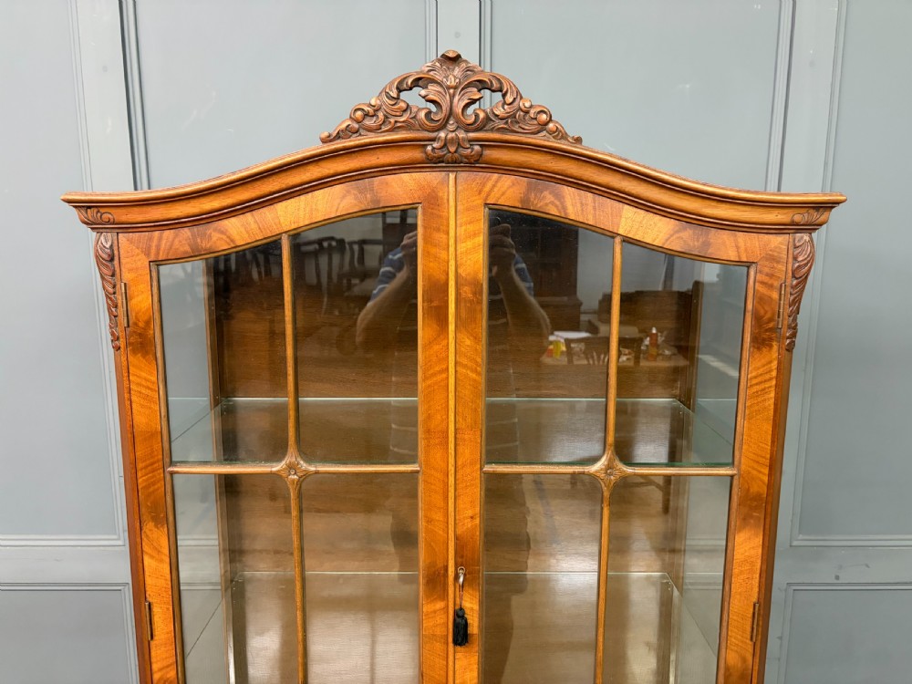 An antique Queen Anne style glazed display cabinet in warm brown wood featuring arched doors with glass panes, drawers with brass handles, and carved cabriole legs. View V