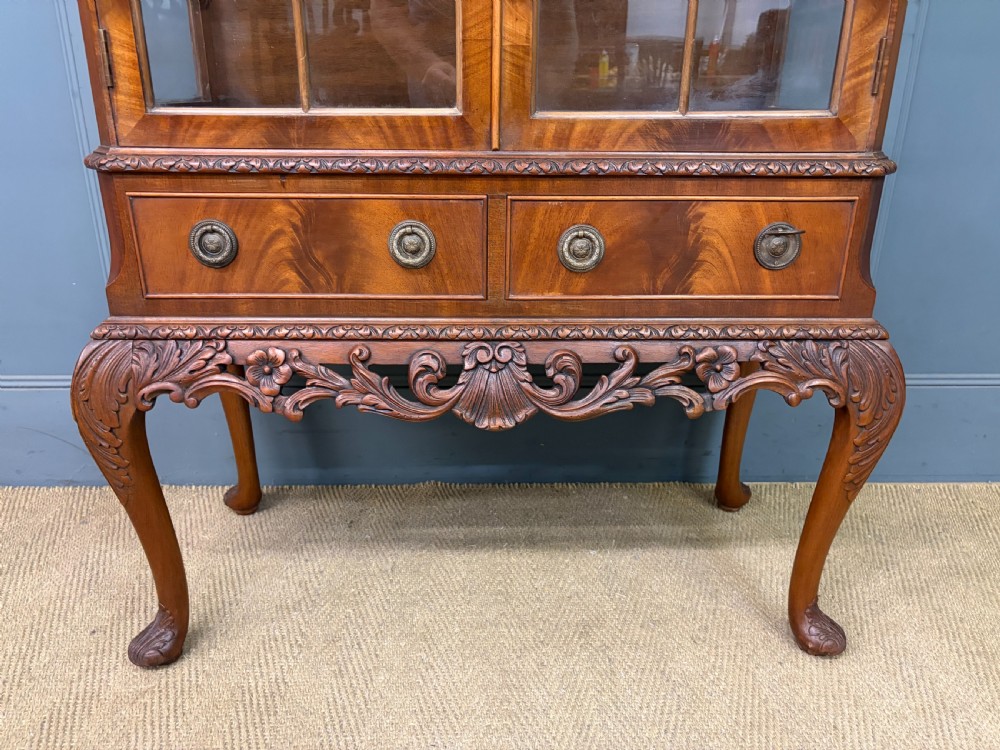 An antique Queen Anne style glazed display cabinet in warm brown wood featuring arched doors with glass panes, drawers with brass handles, and carved cabriole legs. View VI