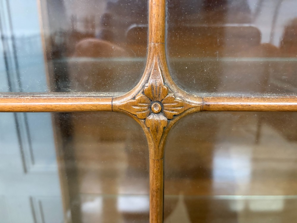 An antique Queen Anne style glazed display cabinet in warm brown wood featuring arched doors with glass panes, drawers with brass handles, and carved cabriole legs. View X
