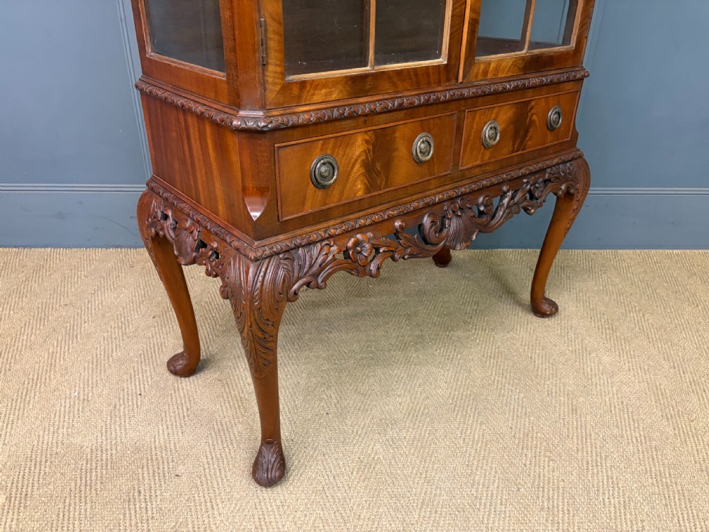 An antique Queen Anne style glazed display cabinet in warm brown wood featuring arched doors with glass panes, drawers with brass handles, and carved cabriole legs. View XV