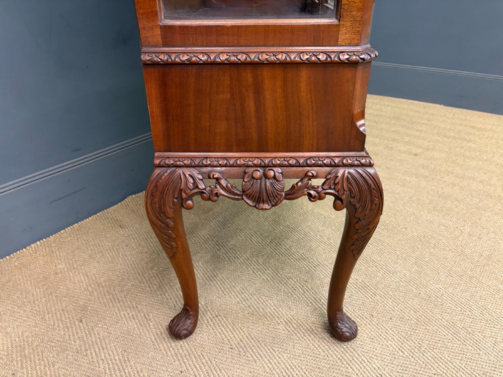 An antique Queen Anne style glazed display cabinet in warm brown wood featuring arched doors with glass panes, drawers with brass handles, and carved cabriole legs. View XVII