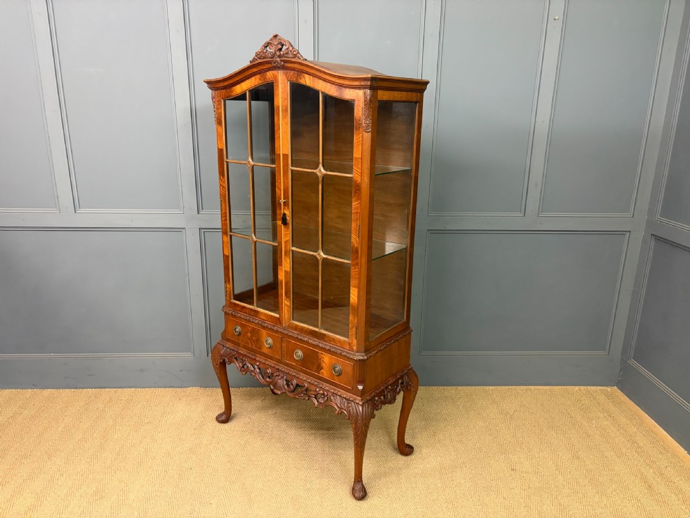An antique Queen Anne style glazed display cabinet in warm brown wood featuring arched doors with glass panes, drawers with brass handles, and carved cabriole legs. View XX