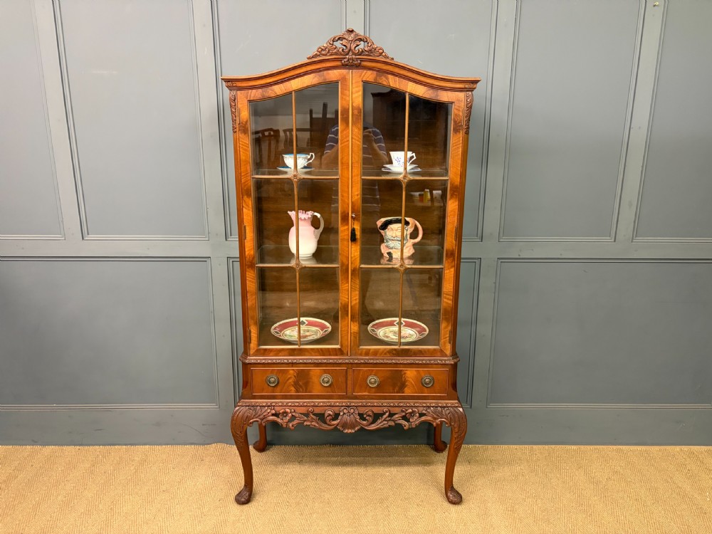 An antique Queen Anne style glazed display cabinet in warm brown wood featuring arched doors with glass panes, drawers with brass handles, and carved cabriole legs. View XXI
