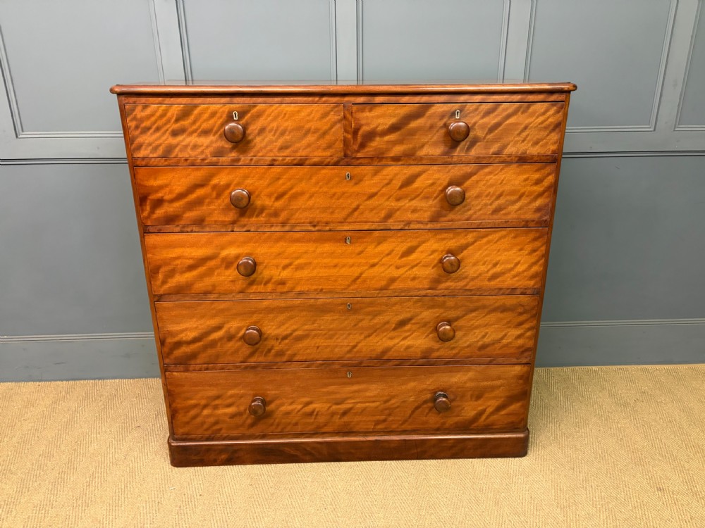 A Victorian chest of drawers in warm brown figured timber featuring turned handles and a plinth base. View IV