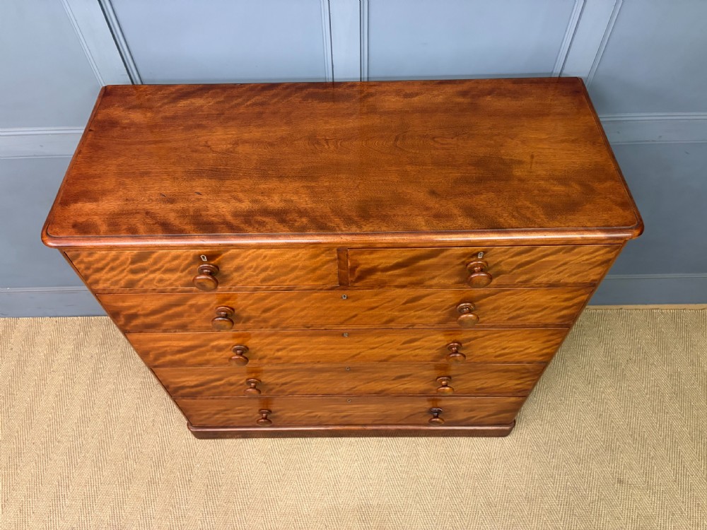 A Victorian chest of drawers in warm brown figured timber featuring turned handles and a plinth base. View V