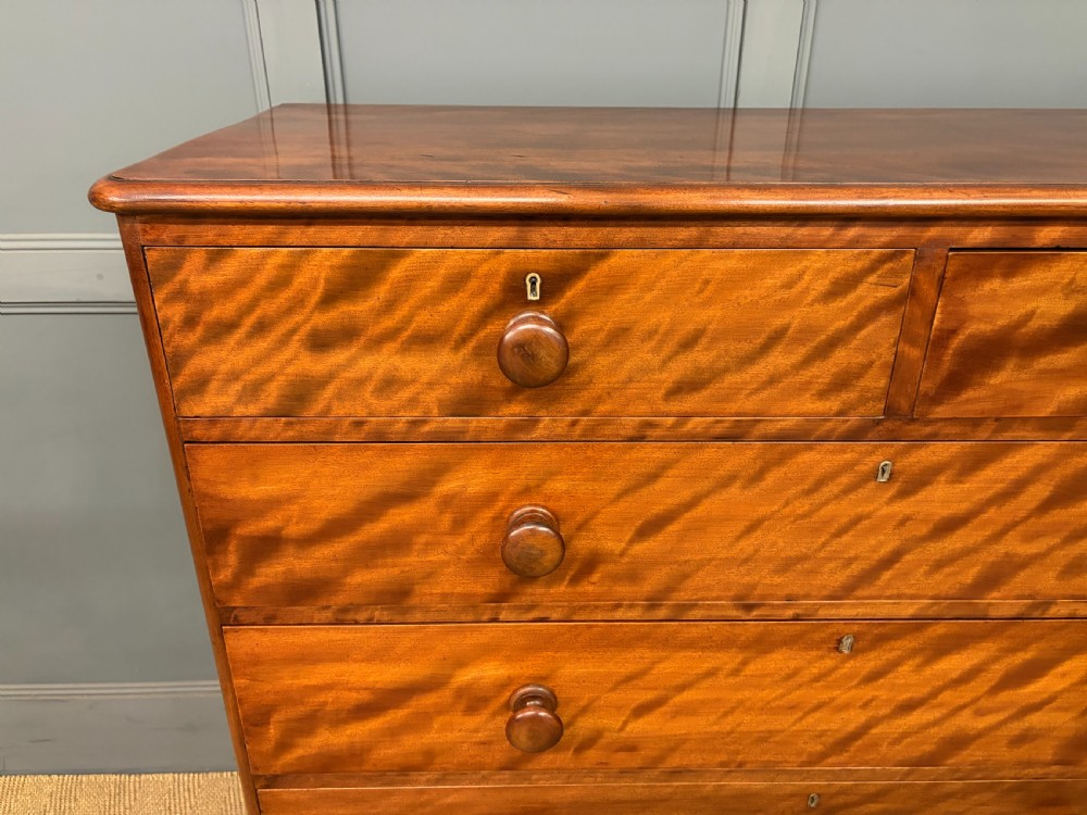 A Victorian chest of drawers in warm brown figured timber featuring turned handles and a plinth base. View VI