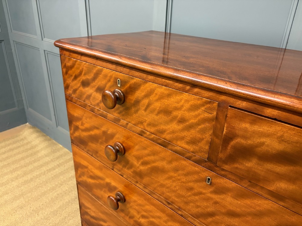 A Victorian chest of drawers in warm brown figured timber featuring turned handles and a plinth base. View VII