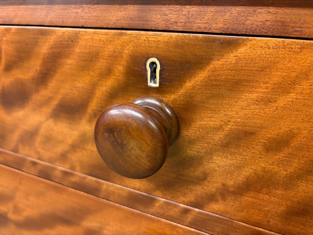 A Victorian chest of drawers in warm brown figured timber featuring turned handles and a plinth base. View VIII